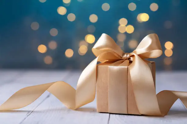 Photo of Christmas or birthday gift box on white wooden table against blue turquoise bokeh lights. Holiday greeting card.