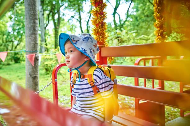 Side view of one cute little boy sitting at red toy children's train.