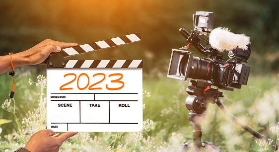 2023- handwritten on film clapperboard. film crew holding film clapperboard and a camera filming a movie in the outdoor background.for creator content in new year