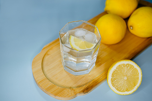 yellow lemons lie on a wooden board with a glass of water on a blue background