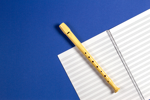 Open exercise book with pentagrams and musical instrument flute on blue background.