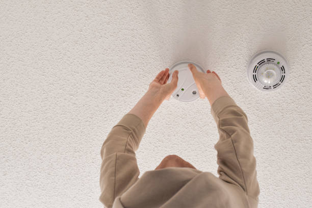 Woman reaching up for smoke alarm on ceiling at home Woman reaching up for smoke alarm on ceiling at home, changing battery time, installation or regular maintenance concept fire inspection stock pictures, royalty-free photos & images