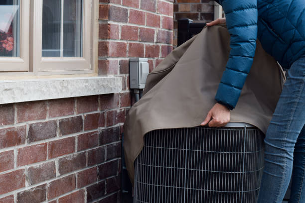 Woman putting cover on air conditioner unit outside the house Woman putting cover on air conditioner unit outside the house in the fall, getting ready for winter, winterizing concept covering stock pictures, royalty-free photos & images
