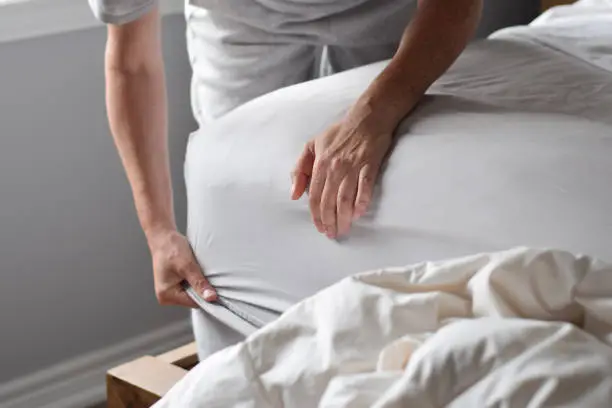 Hands of woman putting on a fitted sheet on a mattress while making the bed