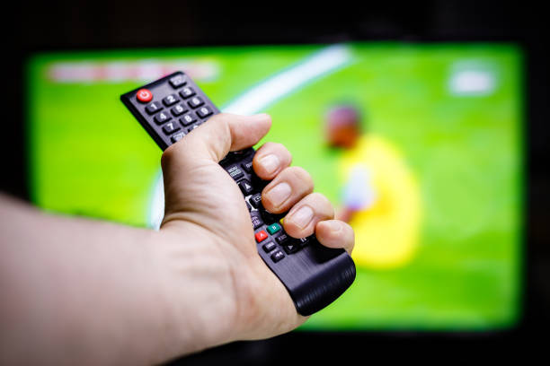 istock Hand-holding TV remote control in front of blurred TV background 1443053498