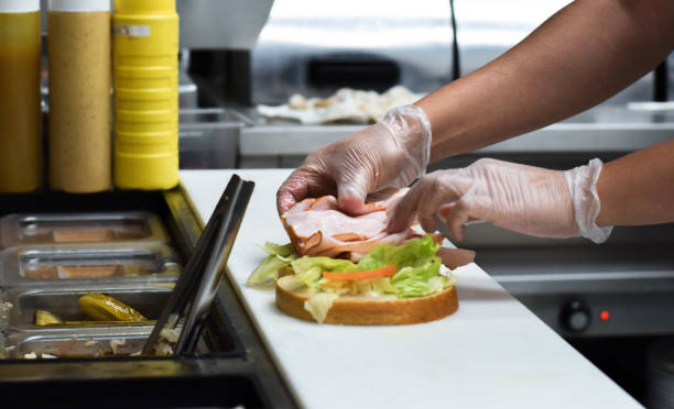Kitchen employee preparing sandwich for customer food order Kitchen employee preparing turkey deli meat sandwich with lettuce for customer food order using protective gloves making a sandwich stock pictures, royalty-free photos & images