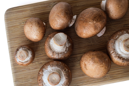 Group of brown cremini mushrooms on wooden cutting board top down view