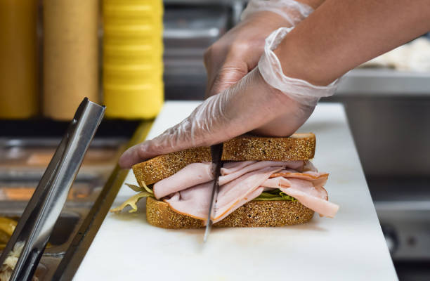 istock Kitchen employee cutting sandwich for customer food order 1443053783