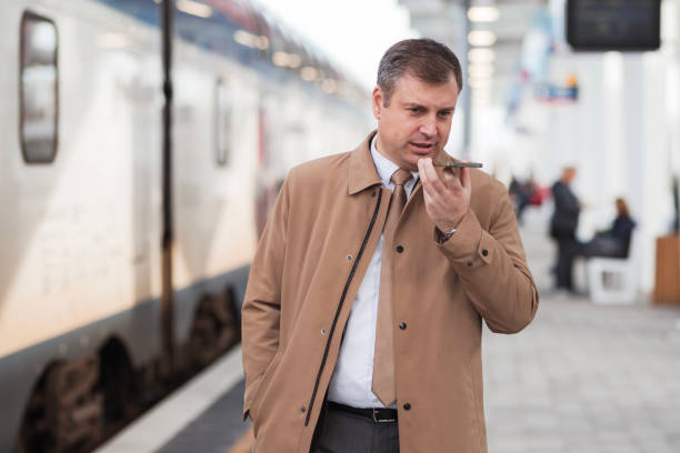 Serious entrepreneur holding phone and recording a voice message on a railroad station