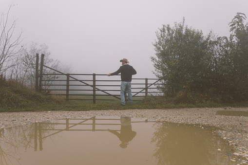 Farmer opening his wooden farm fence gate on foggy autumn day