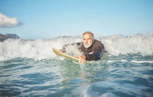 Ocean waves, senior man surfing on beach and healthy fitness lifestyle in Australia summer holiday. Elderly surfer swimming with surfboard, sea water exercise and relax in retirement travel vacation