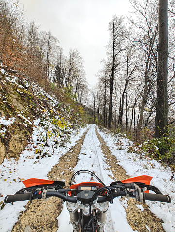 Point of view (POV) of motocross enduro motorbike  handlebars, riding in the winter time on a snow covered dirt road.