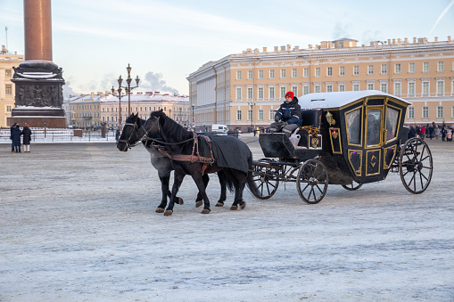 St. Petersburg, Russia - January 08, 2022: A carriage drawn by two black horses on Palace Square. Horse-drawn carriage ride on Palace Square is a romantic attraction for tourists