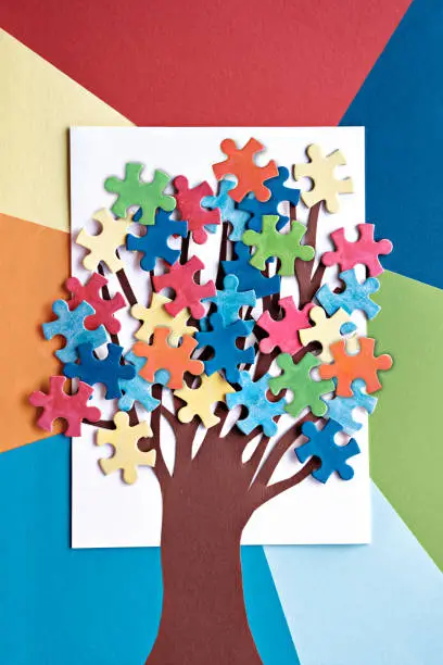 Abstract tree with colorful vibrant puzzle pieces on off white background. Autism Awareness Day, World Autism Day decorative element for banner, wallpaper. Paper art arrangement, creative background for flyer or poster.