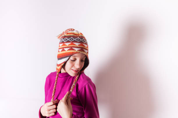 Little child girl wearing knit hat and a red polo neck or roll-neck smiling and looking down on white background