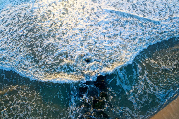 Ocean waves and rocks at water’s edge shot from directly above with camera pointed straight down.