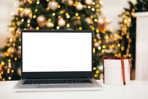 istock Front view of laptop with white screen in home with Christmas tree warm light and gift box. Black Friday discounts. Online shopping. Gifts for the new year and christmas. 1443078673
