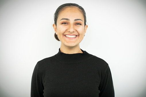 Close up portrait of young adult middle eastern woman with white gray background.