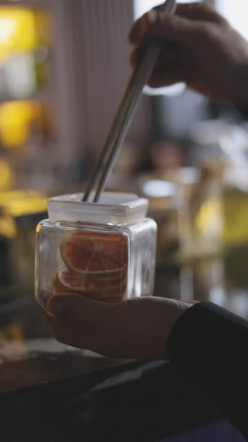 man putting dry grapefruit slices in glass jar, dried fruit slice for cocktail drink, dried grapefruit and orange slice