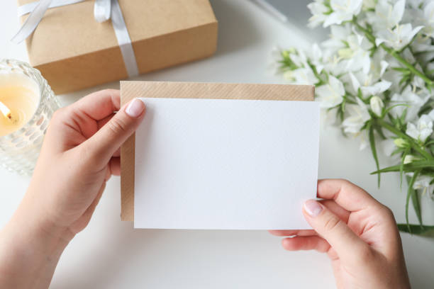 Woman holding envelope with blank greeting card, gift and flowers on the desktop stock photo
