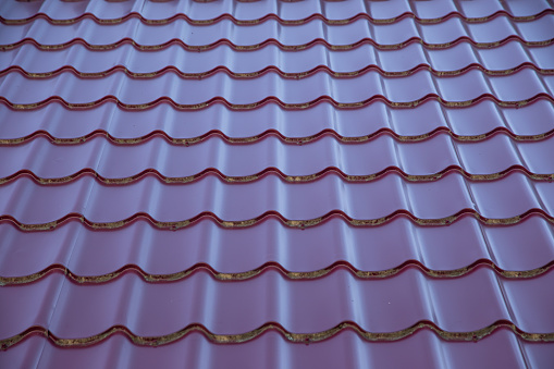 a fragment of a roof with red metal tiles with an attic window, construction