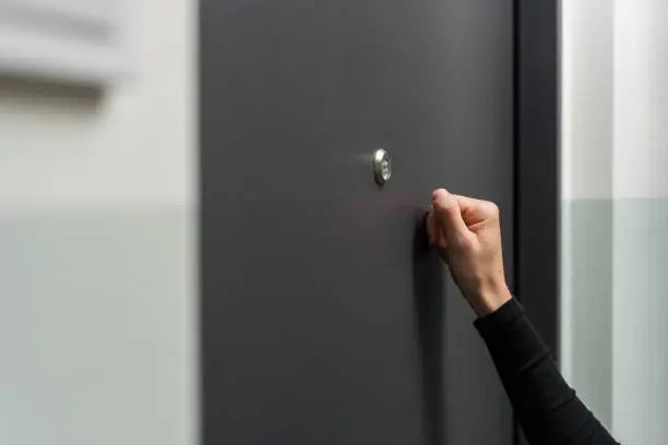 Woman knocking on the metal door standing in the doorway. Side view of female checking noise at neighbors in building. Delivery person, salesperson, hotel service or visitor wants to come in to house