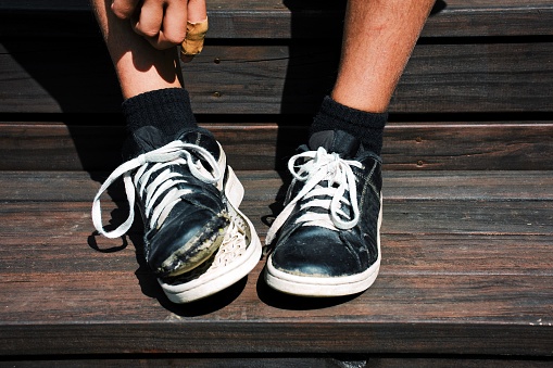 A child wears shoes which are falling to pieces for a poverty concept where parents can no longer afford to buy new shoes for child due to cost of living crisis.