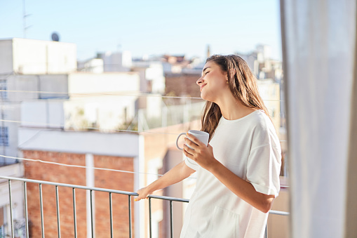 Portrait of a beautiful woman drinking coffee on her balcony in the morning. She has just woken up after a night's sleep.