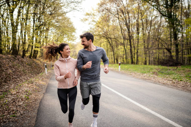 feliz pareja atlética divirtiéndose mientras corre en el día de primavera - correr fotografías e imágenes de stock