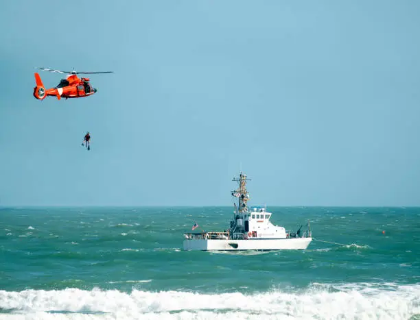 coast guard helicopter lowering diver into the ocean near a coast guard ship