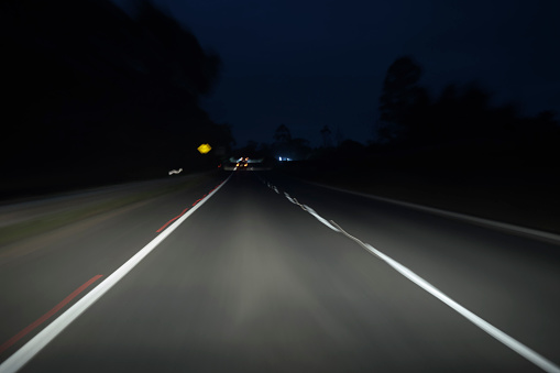 Blurred motion of nighttime driving. Dark road lit by the car headlights. White dividing lines. Left hand driving (eg Australia, UK), flip image horizontally for right hand driving (eg USA).