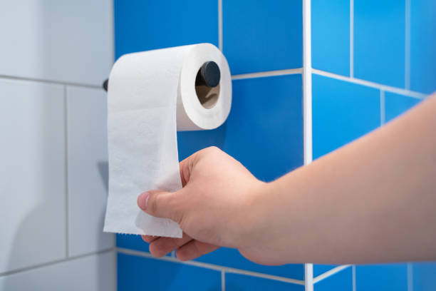 青いタイル張りの壁のトイレにぶら下がっているトイレットペーパーのナプキンロールを持つ手 - paper towel hygiene public restroom cleaning ストックフォトと画像