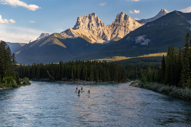 grupo de pessoas remando embarcando no rio bow com as montanhas three sisters ao fundo, canmore, alberta, canadá. - kananaskis country - fotografias e filmes do acervo