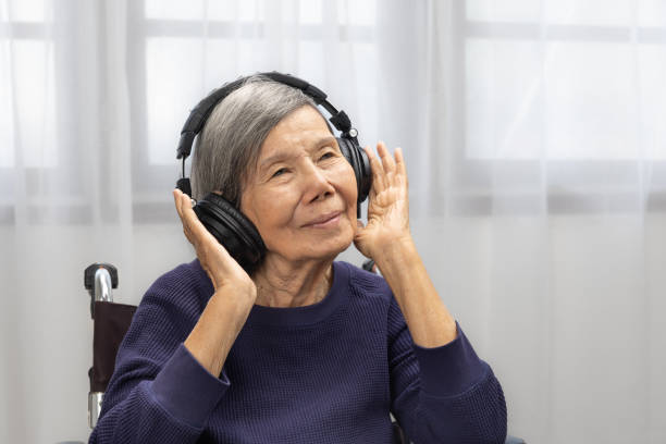 自宅でヘッドフォンで音楽を聴くアジアの年配の女性 - alternative medicine audio ストックフォトと画像