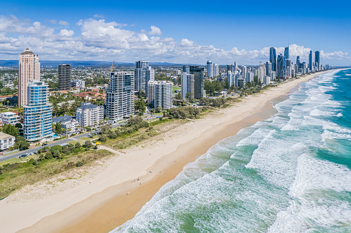 Aerial View Broadbeach towers, Australia's Gold Coast looking north to Surfers Paradise from above the breaking waves. Surf lifesaver (lifeguard) towers with yellow canopies are visible along the wide sandy beach.