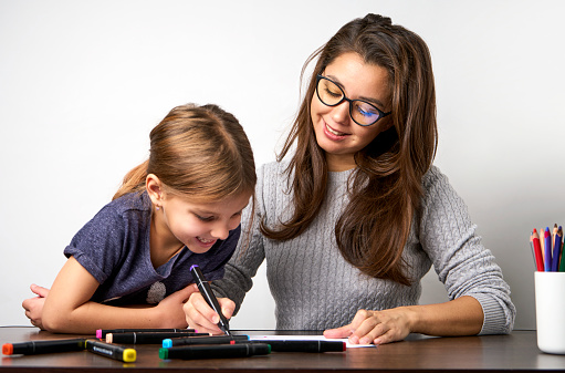 Mother and daughter painting together. Little girl with her mother drawing rainbow. Happy family