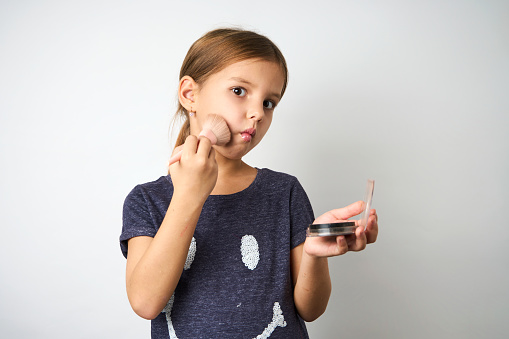 Little girl applying makeup, white background with copy space, close-up