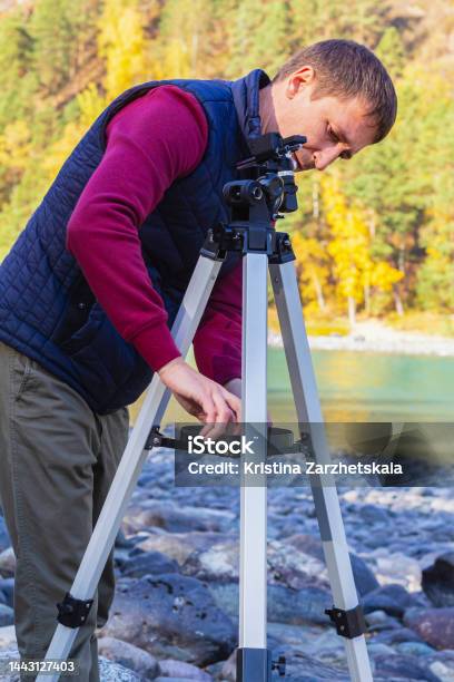 Young Attractive Man Sets Up Metal Tripod Outdoors To Observe Celestial Bodies Through Telescope Stock Photo - Download Image Now