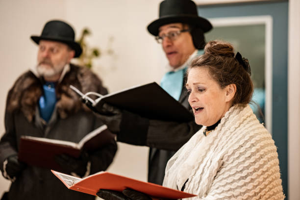 Mature people practising singing for Christmas carolling.  They are dressed up in period costumes. Interior of vintage home during evening.