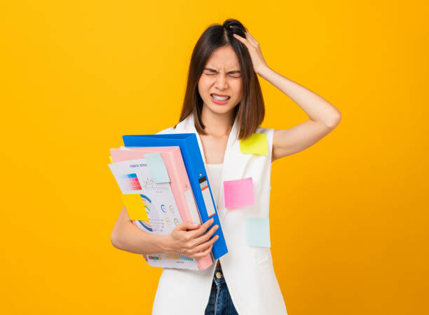 Boring young Asian woman holding document file and a sticky note on the shirt, stand on studio shot yellow background. stock photo