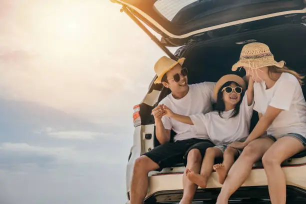 Photo of Dad, mom and daughter enjoying road trip sitting on back car