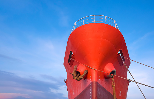 Red Oil Tanker moored at port with mooring rope against blue sky background