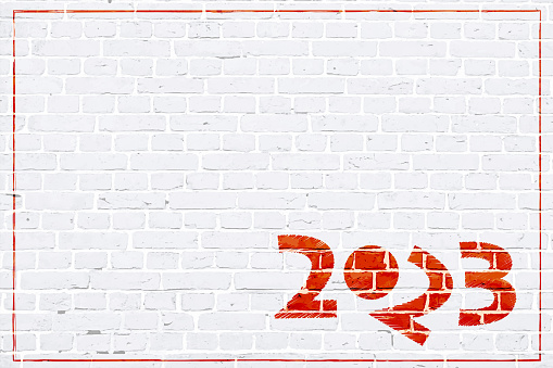 A white colored brick wall textured grunge backgrounds..Text year 2023 in red coloured stroking pattern over white brickwall backdrop with a tilted 2 making the graffiti funny and comic.