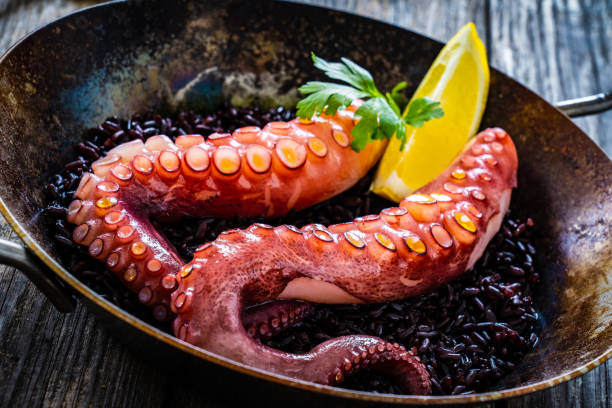 istock Fried octopus with black rice in frying pan on wooden table 1443159080