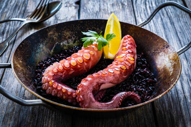 istock Fried octopus with black rice in frying pan on wooden table 1443159090