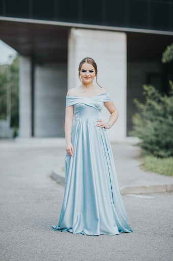 A vertical shot of a Caucasian young female dressed in a beautiful sky-blue floor-length evening gown