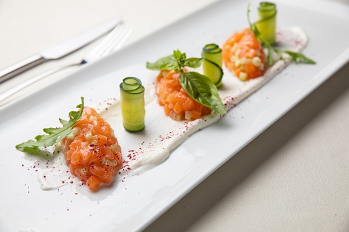 A salmon tartare with avocado and pesto sauce on a white plate.