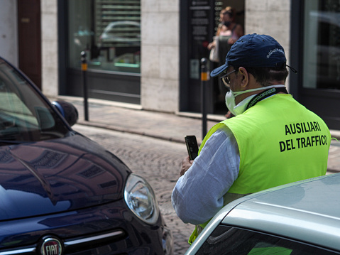 Lombardy, Italy – August 19, 2021: Parking attendant verifying online and issuing printing parking fine in the str
