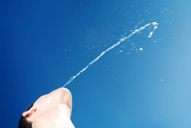 Boy spitting the water jet up to blue, clear sky