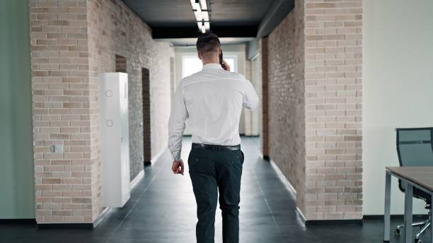 istock Caucasian man on a call while walking in a corridor. Pictured from the back. 1443176155